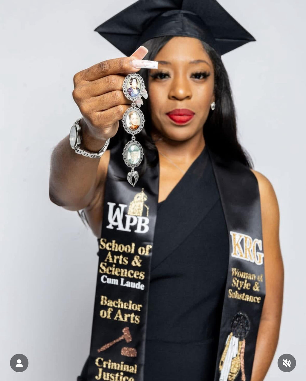 Graduate wearing a handmade, graduation stole/sash, and graduation cap and gown, holding a necklace with a white background