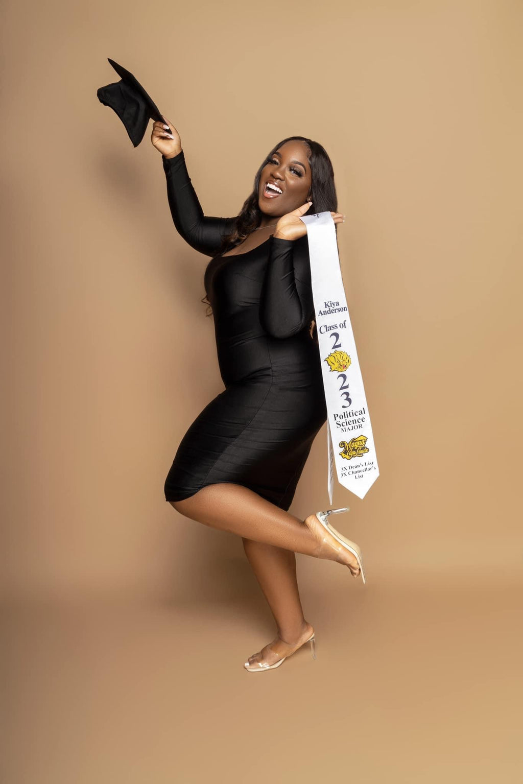 Woman in a black dress holding a sash against a beige background