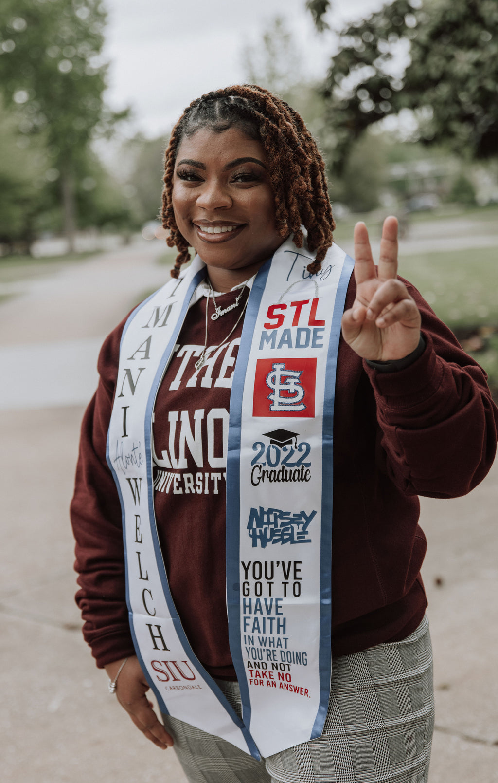 Graduation Pictures wearing a blue and white handmade custom storytelling graduation sash with heat press design for text and logos, outdoors.