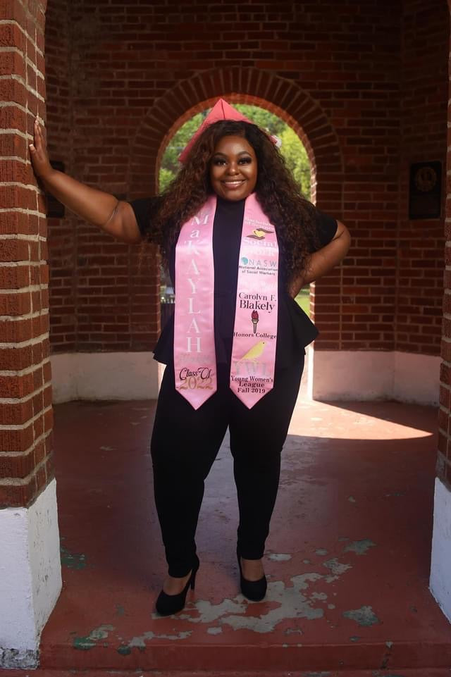 Woman wearing a pink graduation stole in front of a brick archway