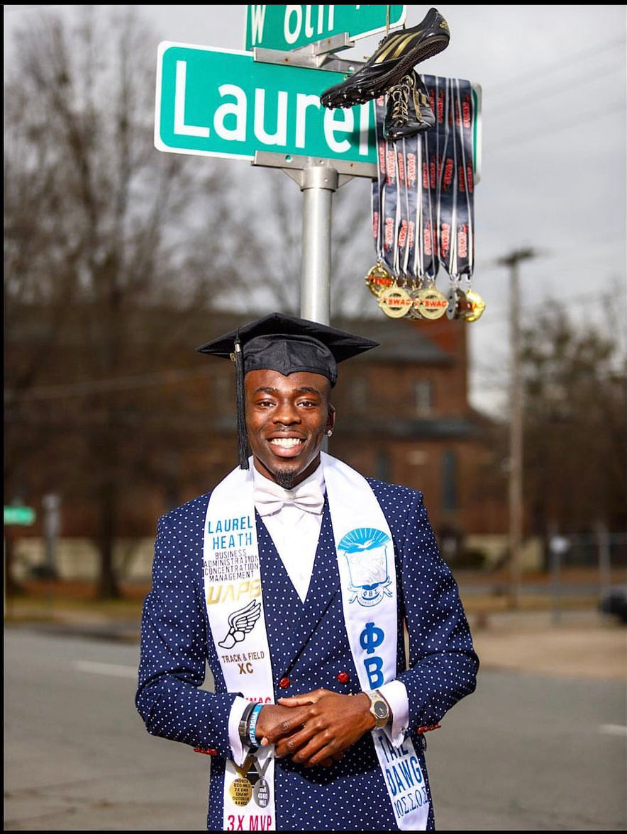 Graduate in cap and gown with stole standing in front of a street sign.