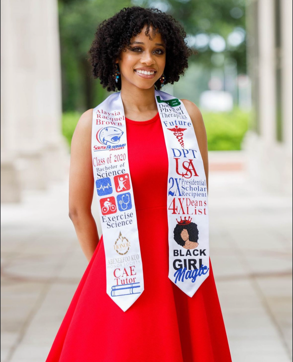 Person wearing a red graduation gown with a colorful stole outdoors.